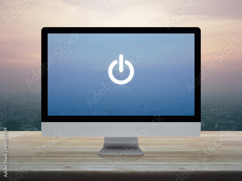 Power button icon on desktop modern computer monitor screen on wooden table over city tower and skyscraper at sunset sky, vintage style, Business start up online concept
