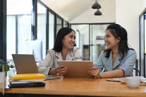 Two young businesswomen using digital tablet and discussing on new startup project together.