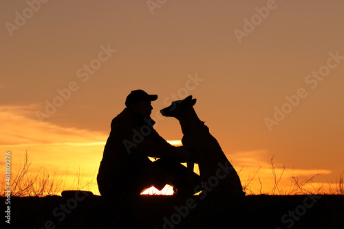 Silhouettes of a man and a dog on a sunset background, the owner walks with his pet in nature, Belgian Shepherd Malinois dog