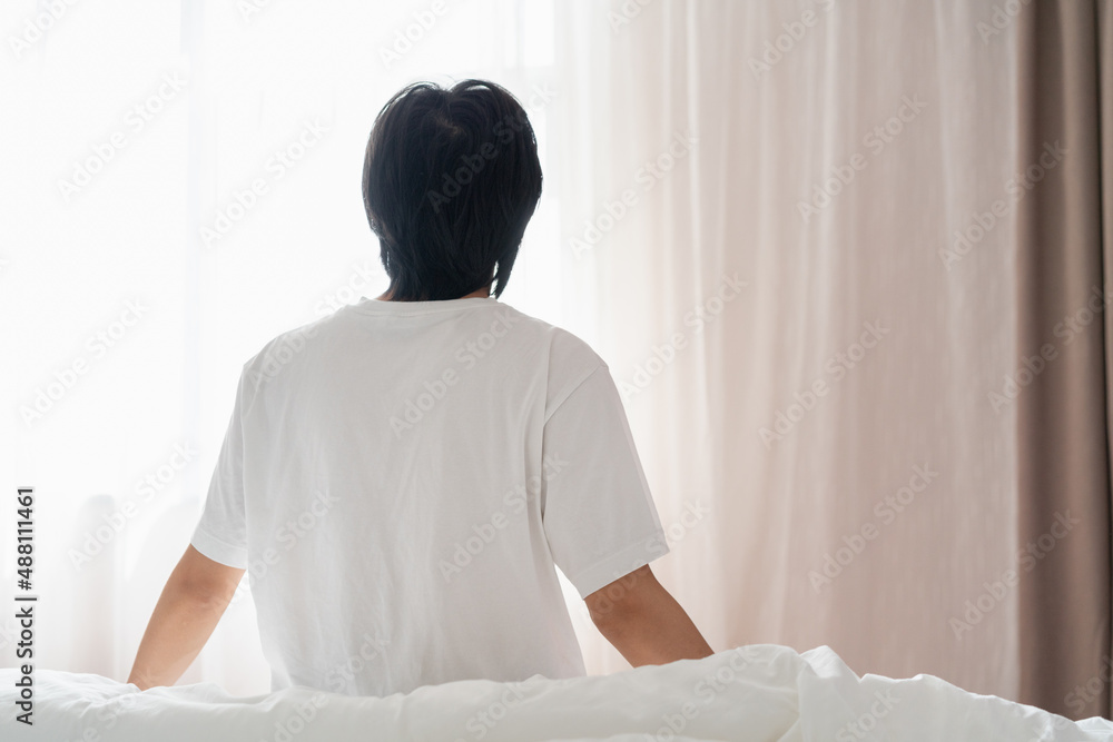 back view of a man sitting on the bed near the window in the morning back view of a man sitting on the bed near the window in the morning