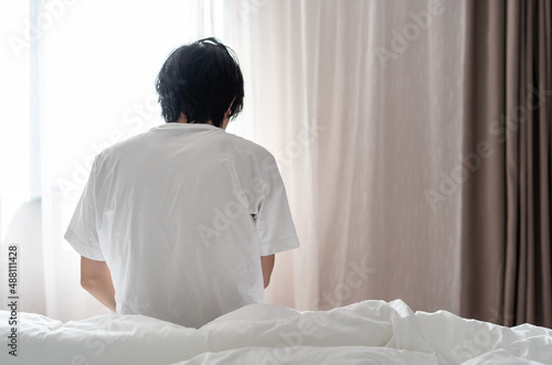 back view of a man sitting on the bed near the window in the morning 