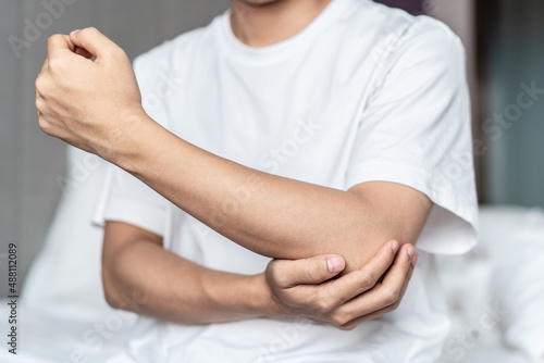 The man sitting in the bed, holding his elbow joint with hands