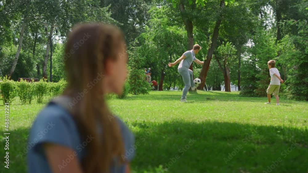 Profile girl watching soccer game in park. Father play football with son. Profile girl watching soccer game in park. Father play football with son.