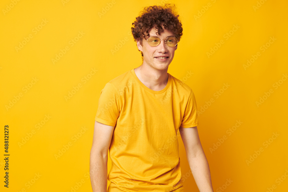 portrait of a young curly man yellow t-shirt glasses fashion hand gestures isolated background unaltered portrait of a young curly man yellow t-shirt glasses fashion hand gestures isolated background unaltered