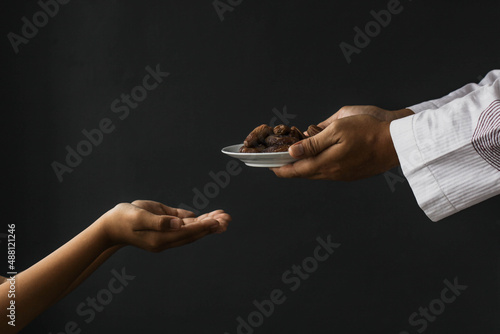 Ramadan kareem concept. Side view Muslim hands giving plate of dates isolated on black background photo