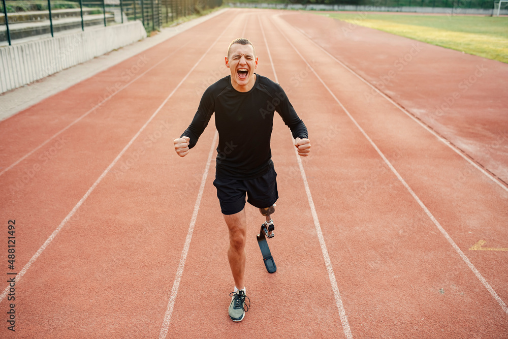A handicapped sportsman with artificial leg standing at stadium and screaming.