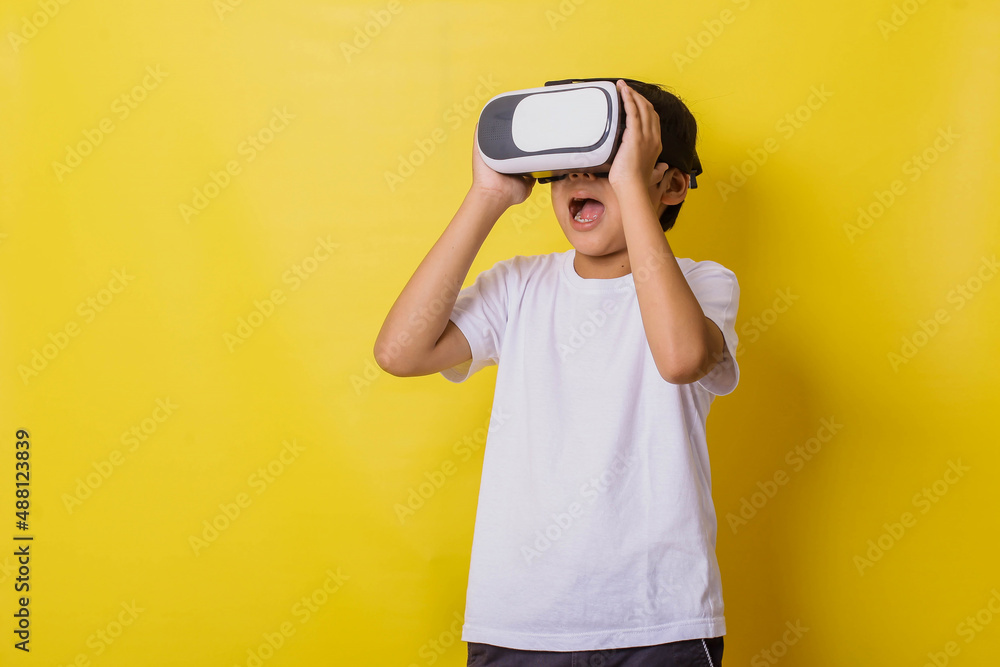 Suprised little boy enjoying playing in virtual reality game isolated on yellow background Suprised little boy enjoying playing in virtual reality game isolated on yellow background