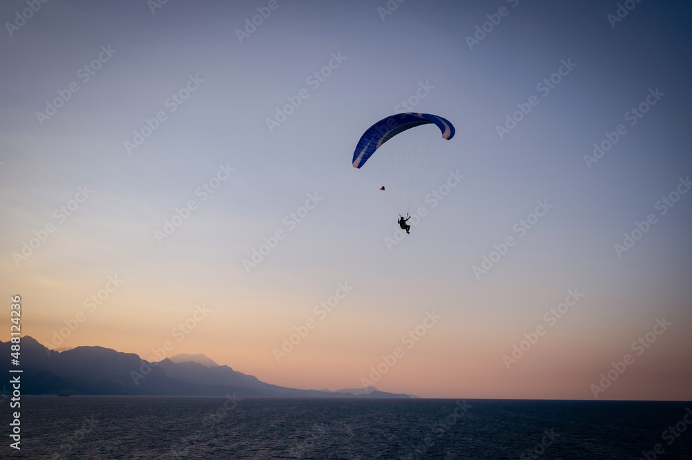 Silhouette of a man on a paraglider flying over the sea at sunset.