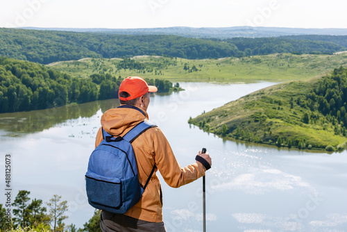  Man standing on top of cliff in summer mountains at sunset and enjoying view of nature.