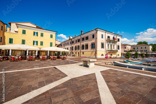 Downtown of Bardolino village, promenade in front of the small port with a restaurant and the town hall. Tourist resort on Lake Garda in Verona province, Veneto, Italy, southern Europe.