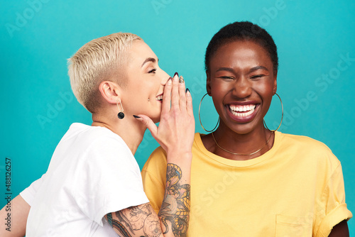 I heard it on the grapevine. Studio shot of a young woman whispering in her friends ear against a turquoise background. photo