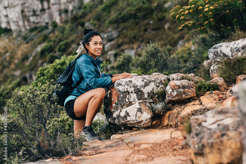 Smiling woman hiker in sports clothes looking away while climbing rock