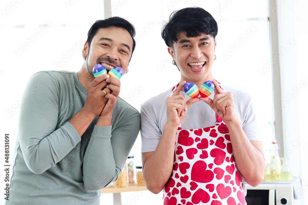 Happy young LGBT couple holding rainbow Easter eggs that are symbol of LGBTQ flag color, Asian gay male lover sharing special moment together to celebrate Easter holiday. Happy young LGBT couple holding rainbow Easter eggs that are symbol of LGBTQ flag color, Asian gay male lover sharing special moment together to celebrate Easter holiday.