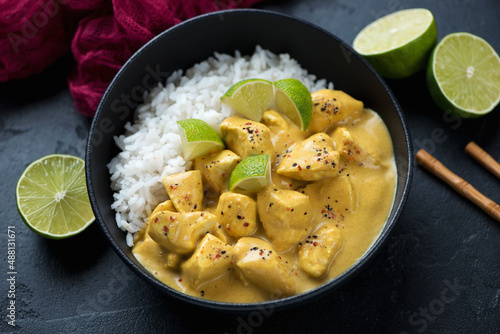 Bowl of yellow curry with chicken meat and white rice, studio shot on a black stone background, middle close-up