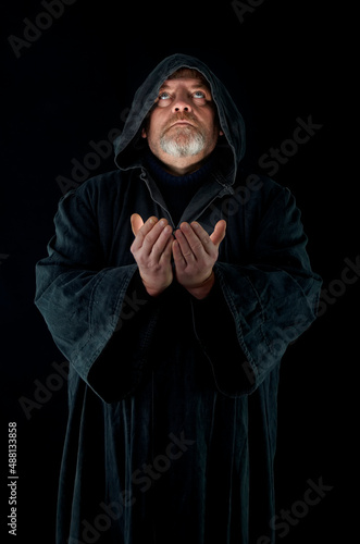 Bearded man in a monk's cloak prays on a black background