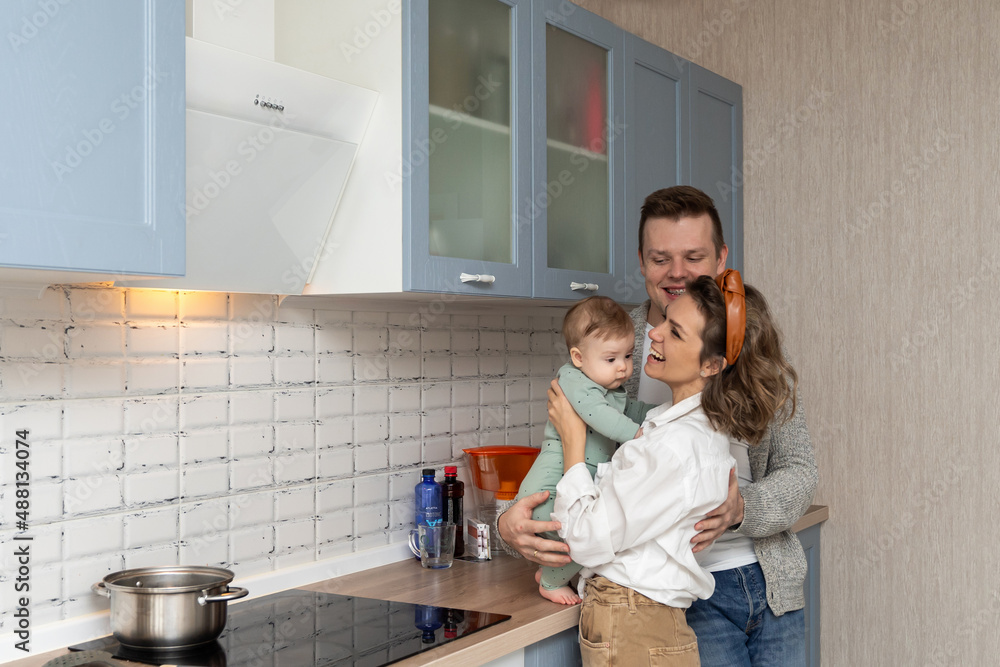Young happy family Father mother baby cooking dinner together in kitchen. Home casual concept. Parenthood. Home recreation and food preparation on weekend Young happy family Father mother baby cooking dinner together in kitchen. Home casual concept. Parenthood. Home recreation and food preparation on weekend