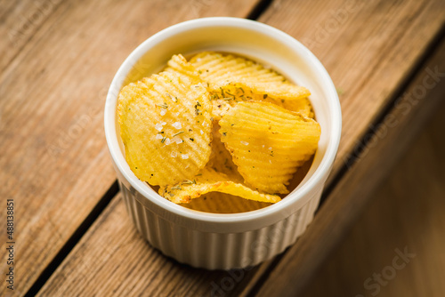 Salty grooved chips in white ceramic bowl on the rustic background. Selective focus. Shallow depth of field.