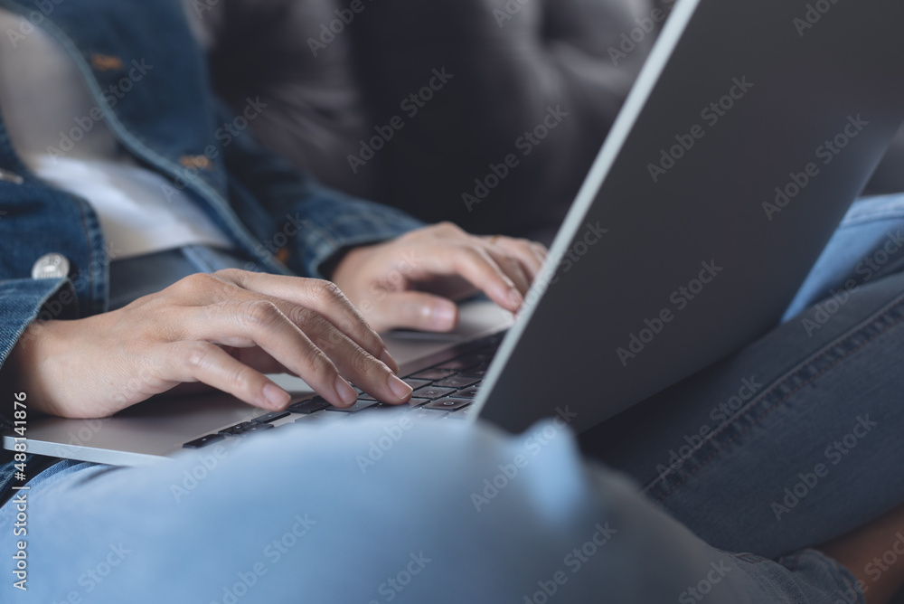 Fototapeta premium Young woman sitting on sofa, working and typing on laptop computer at home, working at home, telecommuting concept