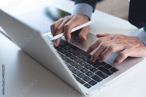 Close up of businessman working on laptop computer and using digital tablet on white office table