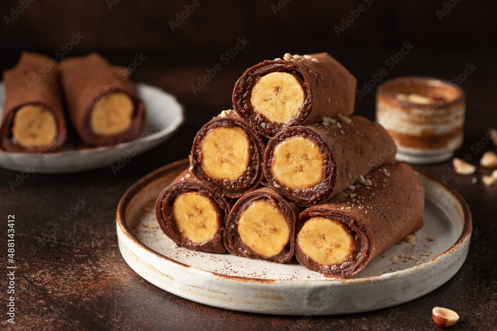 Rolled vegan chocolate crepes with banana filling on dark background. vegan thin pancakes for breakfast or dessert Rolled vegan chocolate crepes with banana filling on dark background. vegan thin pancakes for breakfast or dessert