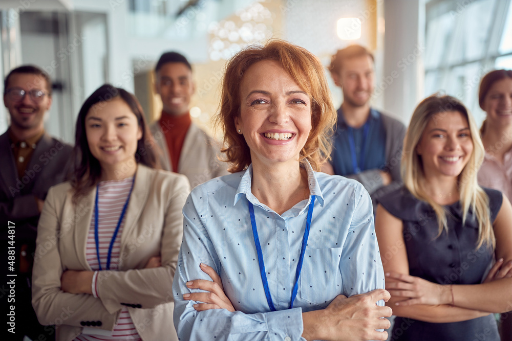 Close-up shot of cheerful female manager and her young team standing in the company building hallway and posing for a photo. Business, people, company Close-up shot of cheerful female manager and her young team standing in the company building hallway and posing for a photo. Business, people, company
