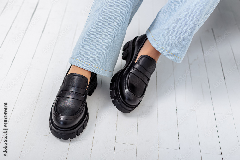 A young woman with slender beautiful legs in fashionable black leather shoes  sits on a chair in the studio. Women's stylish loafers, close-up. Spring  shoe collection Stock Photo | Adobe Stock