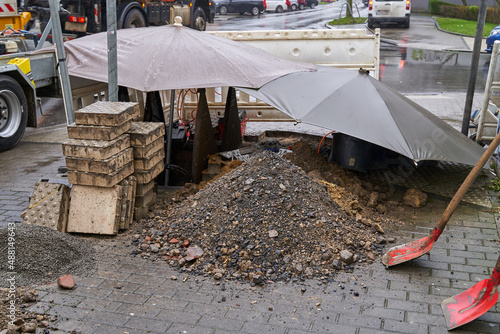 Open construction site on a rainy day covered with umbrellas. Shovels and stone blocks are visible.