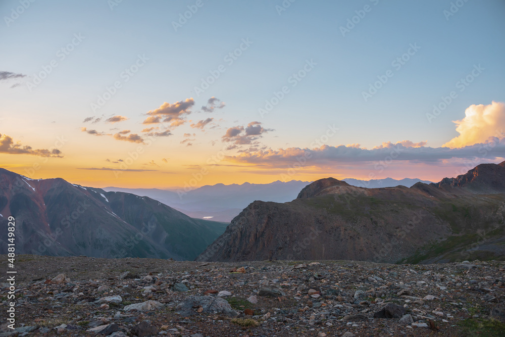 Atmospheric alpine landscape with large mountains in orange dawn sky. Colorful top view to high mountain range under cloudy sky in sunset colors. Awesome mountain sunset scenery at very high altitude.