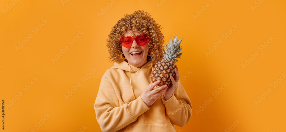Beautiful 20s woman in bright sunglasses with pineapple posing on yellow color background. Health and diet concept.