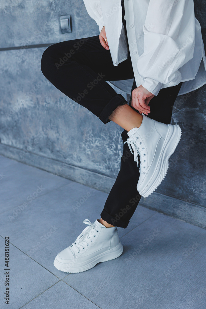 Women's legs in black trousers and white leather sneakers. Modern casual style. New shoe collection