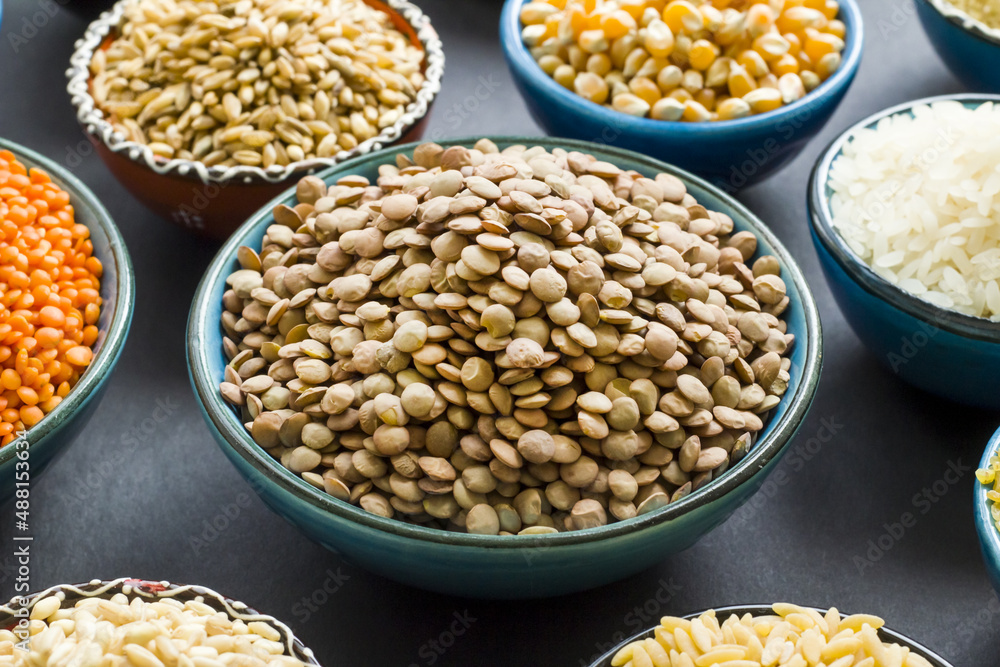 Uncooked dry cereal food group in ceramic bowls on black surface.Selected green lentil bowl Uncooked dry cereal food group in ceramic bowls on black surface.Selected green lentil bowl