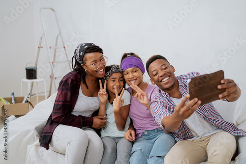 Cheerful family renovates a new apartment  laughing father takes a selfie with his wife and children  daughters fool around  pose for a photo  a funny team  a ladder in the background  cardboard boxes