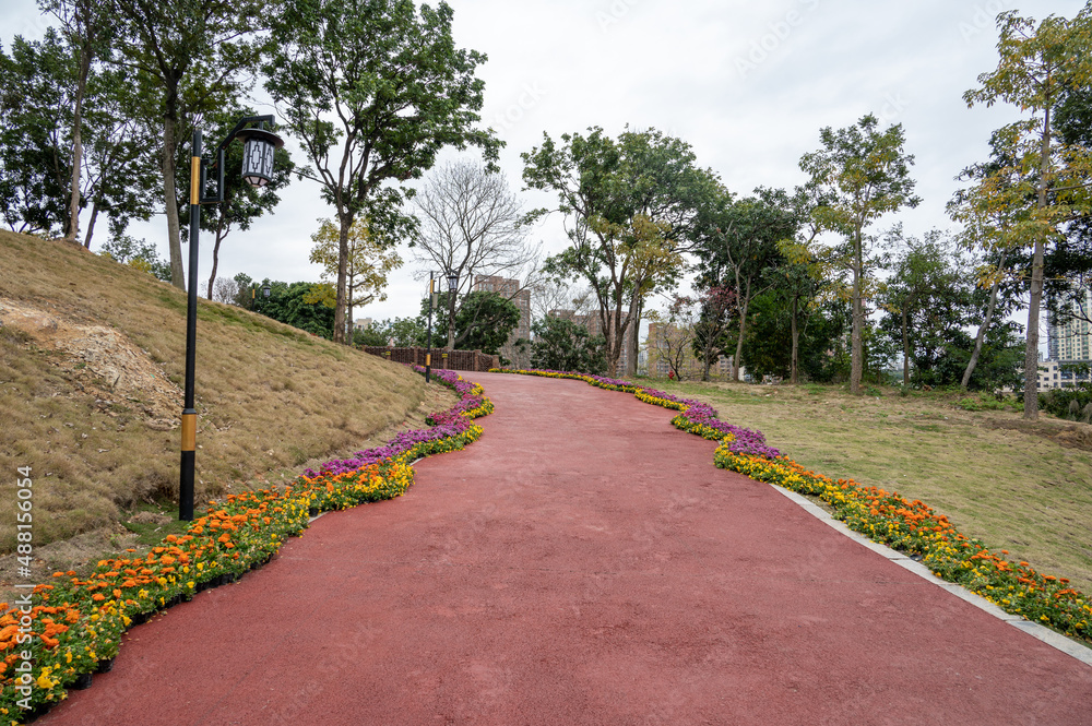 The red asphalt runway in the modern city park is surrounded by green plants on both sides