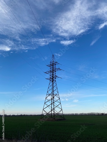 Vertical shot of a transmission tower in green field under blue sky