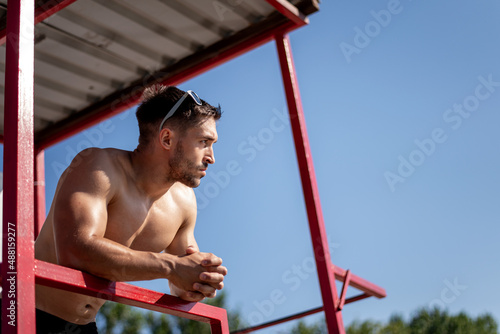 Shirtless muscular man in sunglasses on a beach.