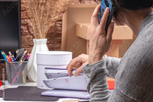 Woman talking with client on the phone, recieve orders, working in her workplace at home. Startup small business freelance workspace, handmade craft, self employed, small family business concept