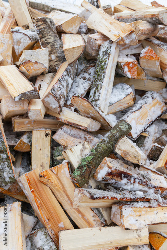 Chopped birch firewood lies in a heap on the snow in winter
