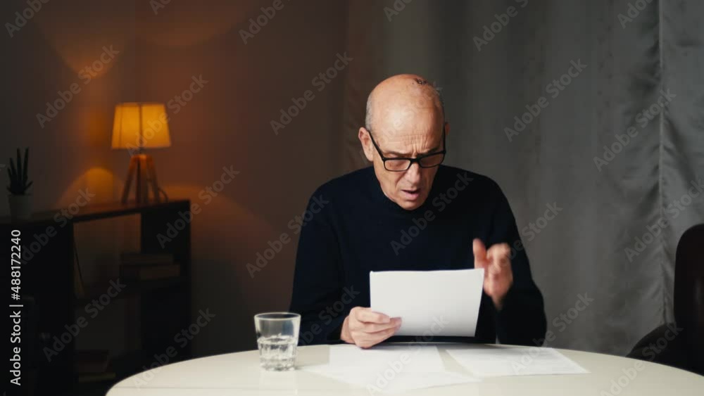 Elderly man sitting at the table reads his electricity and gas bills Elderly man sitting at the table reads his electricity and gas bills