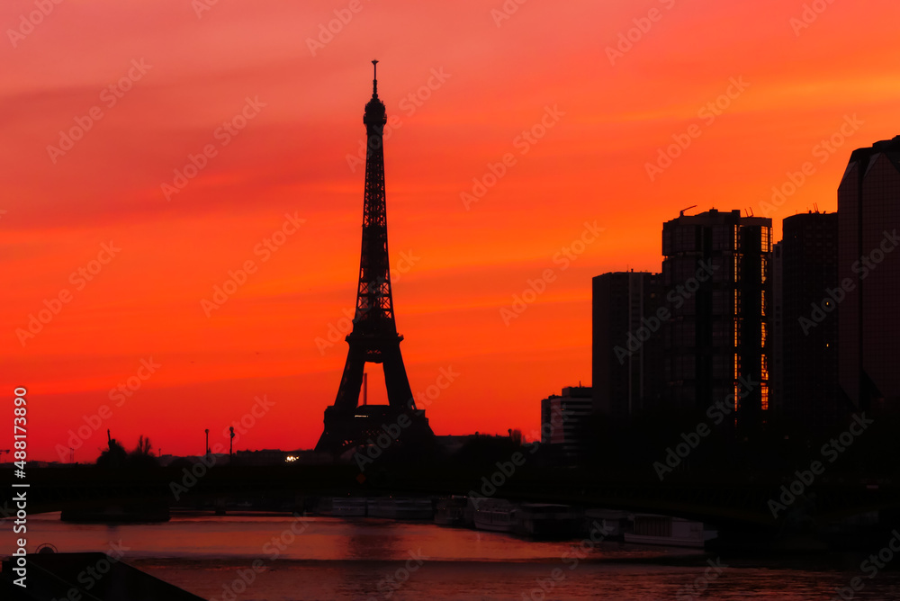 Urban landscape. View on the Eiffel tower with group of modern buildings in front of the water of Seine river. Dramatic sky with colorful clouds. Silhouette of a cityscape at sunrise.
