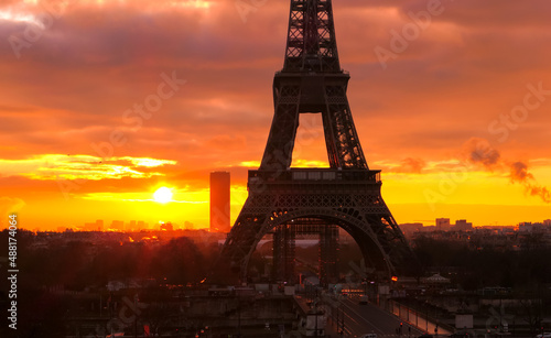 View on the Eiffel tower of Paris at sunrise or sunset. Dramatic sky with sunlight and cumulonimbus. Historic monument.