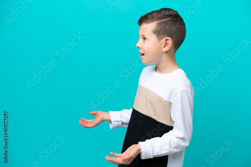 Little kid boy isolated on blue background with surprise expression while looking side