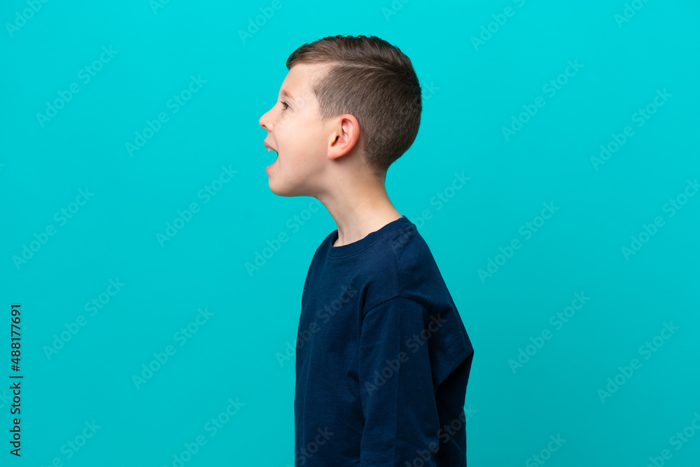 Little kid boy isolated on blue background laughing in lateral position Little kid boy isolated on blue background laughing in lateral position