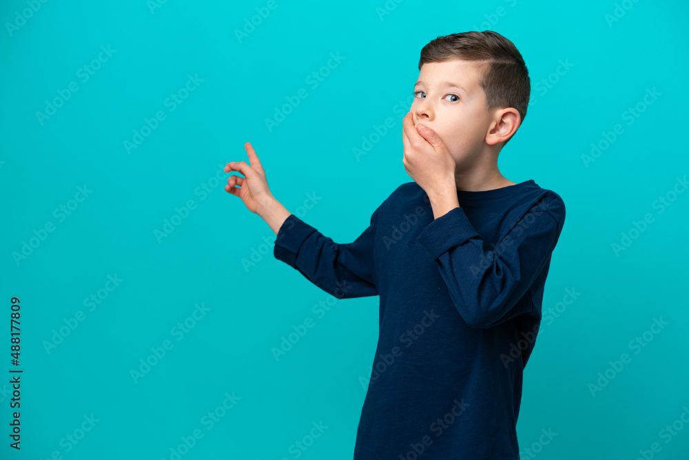 Little kid boy isolated on blue background with surprise expression while pointing side Little kid boy isolated on blue background with surprise expression while pointing side