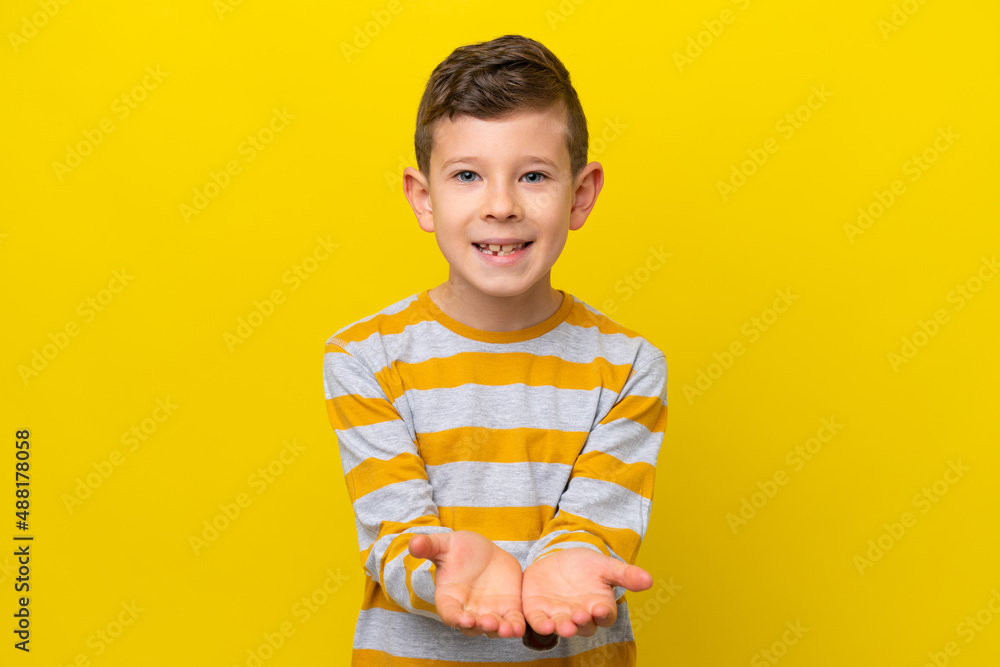 Little caucasian boy isolated on yellow background holding copyspace imaginary on the palm to insert an ad Little caucasian boy isolated on yellow background holding copyspace imaginary on the palm to insert an ad
