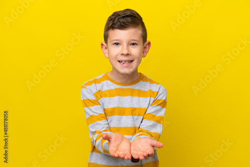 Little caucasian boy isolated on yellow background holding copyspace imaginary on the palm to insert an ad