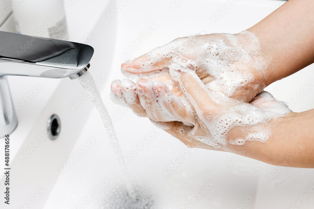 Fototapeta premium Young woman washing hands under streaming water from faucet with soap in bathroom, hygiene concept