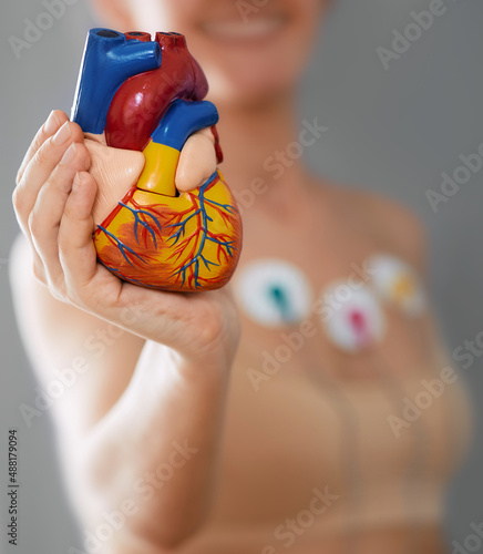 Heart health concept, cardiac stress test. Woman during heart test with sensors holds anatomical model of human heart in hand in front of her photo