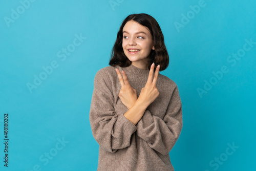 Teenager Ukrainian girl isolated on blue background smiling and showing victory sign