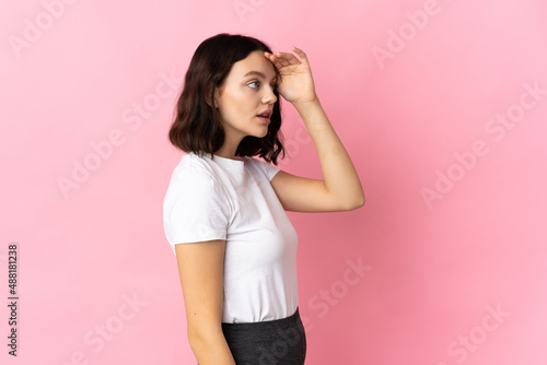 Teenager Ukrainian girl isolated on pink background with surprise expression while looking side