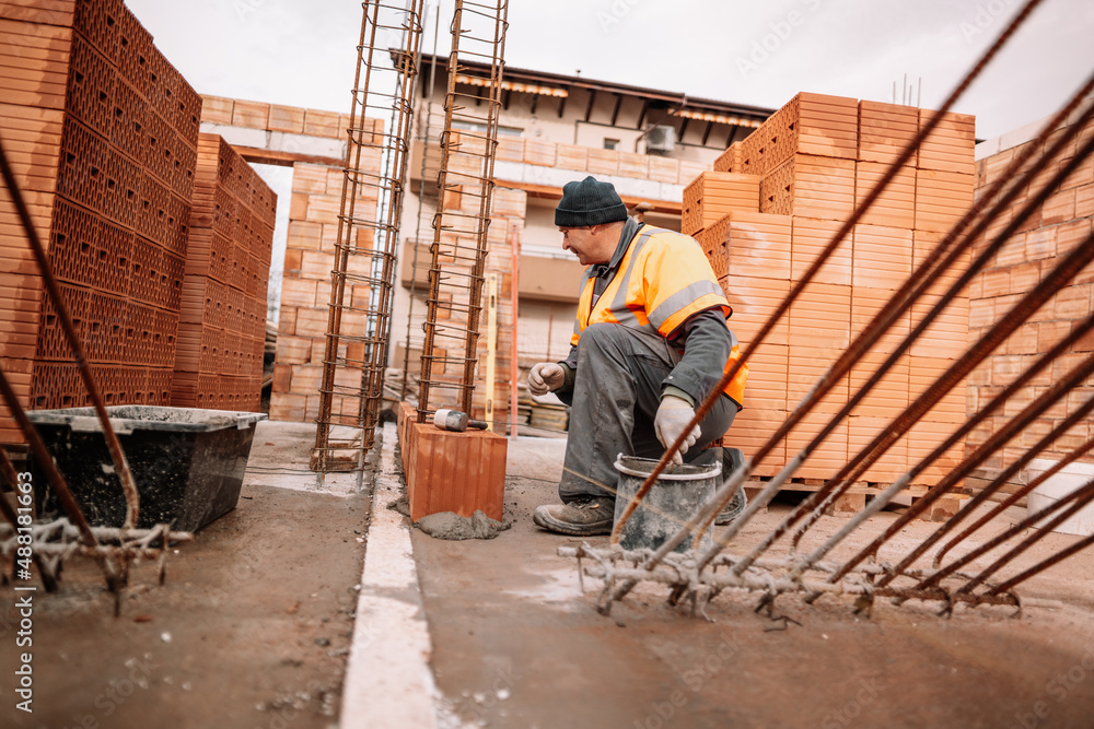 Fototapeta premium Industrial worker using trowel and tools for building exterior walls with bricks and mortar